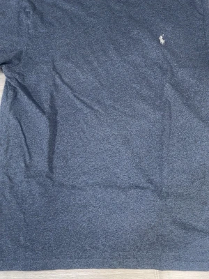Blå tröja från Polo Ralph Lauren - Mörkblå tröja från Polo Ralph Lauren med klassisk v-ringning och den ikoniska vita polospelaren broderad på bröstet. Tröjan är i mjukt material och har en enkel, stilren design som passar perfekt till jeans eller chinos.