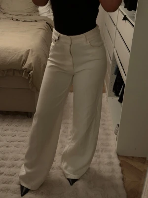 Vida vita jeans med hög midja - Säljer ett par snygga vita jeans med hög midja och vida ben. Jeansen har klassisk femficksmodell och stängs med dragkedja och knapp. Perfekta för en clean och trendig look.