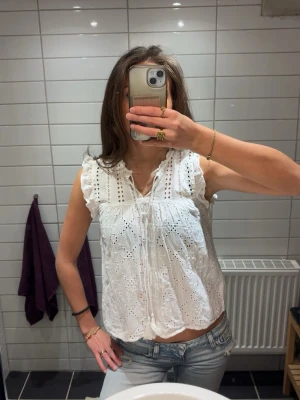 Vit broderad blus - Söt vit ärmlös blus från ONLY med broderade detaljer och volang vid axlarna. Blusen är något mindre i storleken och är inte strykt på bilderna tyvärr. Använd en gång, pris kan diskuteras.