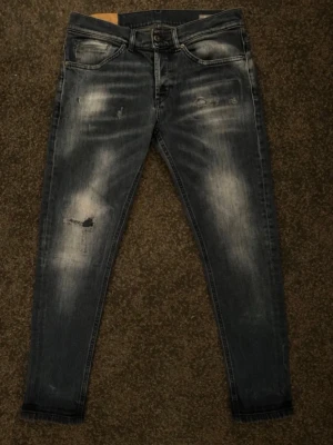 Dondup jeans - Säljer ett par grå skinny jeans med slitningar och tvättade detaljer. Jeansen har fem fickor, knappgylf och smal passform. Materialet är klassisk denim med stretch för extra komfort. Perfekta för en avslappnad och trendig look.