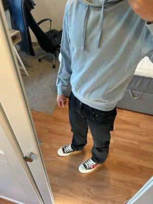 Ljusblå hoodie från Hugo Boss - Säljer en stilren ljusblå hoodie från Hugo Boss med klassisk huva och dragsnören. Hoodien har ribbade muddar vid ärmslut och nederkant samt en relaxed passform. Perfekt för dig som gillar enkel och clean streetwear.