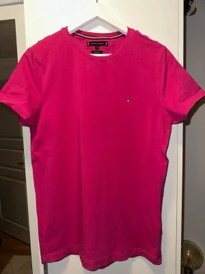 Rosa t-shirt från Tommy Hilfiger - Snygg rosa t-shirt från Tommy Hilfiger med extra slim fit passform. Klassisk rund halsringning och diskret logga broderad på bröstet. Tillverkad i mjuk bomull som känns skön mot huden. Perfekt för dig som gillar stilrena och färgstarka plagg.