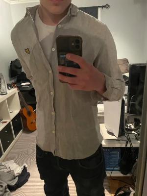 Beige linne skjorta från Lyle & Scott - Säljer en beige linne  skjorta från Lyle & Scott med klassisk krage och långärmad design. Skjortan har knappar framtill och en bröstficka med den ikoniska Lyle & Scott-loggan. Perfekt för dig som vill ha en stilren och enkel look. Perfekt till sommaren! Storlek M men sitter som S. Helt ny oanvänd 