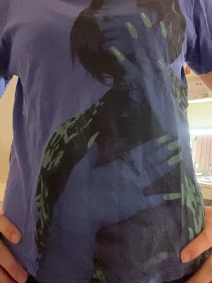 Blå Billie Eilish t-shirt med grafiskt tryck - Cool blå Billie Eilish t-shirt med stort grafiskt tryck av Billie Eilish med neongröna naglar på framsidan. T-shirten har rund hals och korta ärmar.