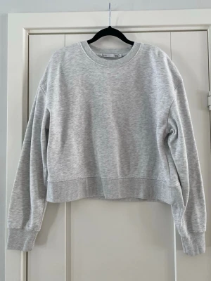 Grå croppad sweatshirt - En enkel och stilren ljusgrå sweatshirt med croppad passform och rund hals. Tröjan har långa ärmar och ribbade muddar vid ärmslut och nederkant. Perfekt för en avslappnad och trendig look. Använd lite små noppor i övrigt i fint begagnat skick  Mått Över bröstet: ca 57 cm Längd från axeln och ner: ca 53 cm  99% bomull och 1% viskos  Kommer från ett djur och rökfritt hem