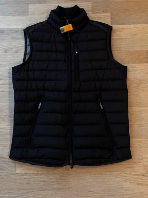 Svart dunväst från Parajumpers - Snygg svart dunväst från Parajumpers med gul detalj vid kragen och tre dragkedjeförsedda fickor. Västen har quiltad design och hög krage, perfekt för lager på lager under kyliga dagar.