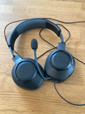JBL Quantum 100 Gaming Headset - Säljer ett svart JBL gaming headset med inbyggd mikrofon och vadderad bygel. Hörlurarna har stora, mjuka öronkuddar och tydliga L/R-markeringar på insidan. Sladden är tygklädd för extra hållbarhet och headsetet har en modern, robust design. Nypris: 400kr. Mitt pris: 199
