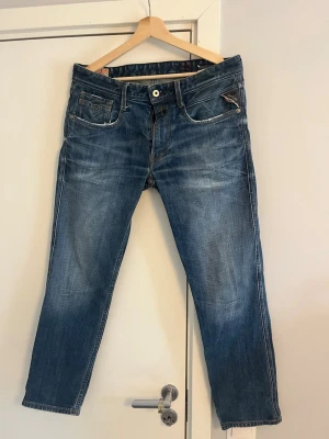 Replay jeans - Säljer ett par blå jeans från replay med klassisk femficksdesign och raka ben. Jeansen har snygga slitningar och kontrastsömmar, samt en liten logodetalj på fickan. Materialet är denim och passformen är avslappnad. Dom är storlek 33x32
