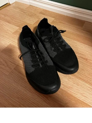 Svarta stickade sneakers med snörning - Snygga svarta sneakers med grå detaljer och stickad ovandel. Skorna har klassisk snörning och en låg profil som ger en sportig look. Perfekta för dig som gillar stilrena och bekväma skor till vardags. Materialet är mesh-liknande och sulan är i gummi.