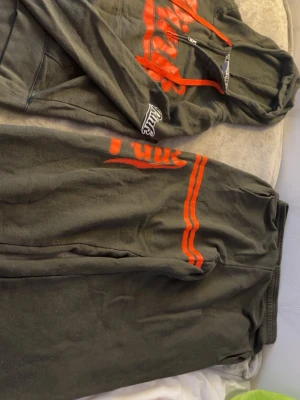 Grått/grönt loungewear-set från Pink - Mysigt loungewear-set från Pink i mjuk grå bomullsblandning. Setet består av en hoodie med halv dragkedja, röda detaljer och tryck samt matchande byxor med röda ränder och logga. Perfekt för chill dagar hemma. Men lite nopprigt.