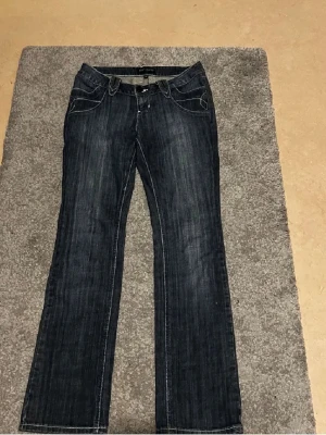 Mörkblå bootcut jeans från L.O.G.G. - Snygga mörkblå bootcut jeans från L.O.G.G. Med 2000-talet mode,  med dekorativa detaljer på bakfickan och kontrastsömmar. Klassisk femficksmodell i slitstark denim med lätt tvättad look. Perfekta för en avslappnad och trendig stil. 