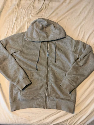 Grå zip hoodie från Burberry - Snygg grå hoodie från Burberry med dragkedja framtill, två fickor och justerbar huva med snören. Klassisk och enkel design med ribbade muddar och diskret Burberry-detalj på snörändarna. Perfekt för en chill och stilren look.