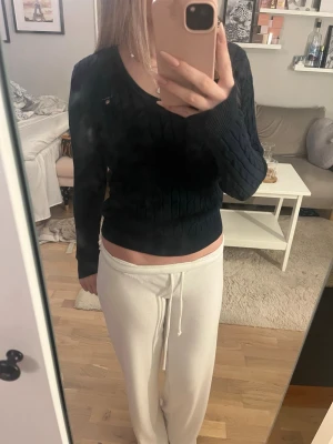 Mörkblå kabelstickad tröja Gant - Snygg mörkblå kabelstickad tröja från Gant med V-ringning och diskret logga på bröstet. Tillverkad i bomull och har långa ärmar samt ribbade muddar. Perfekt till jeans eller kjol för en klassisk look.