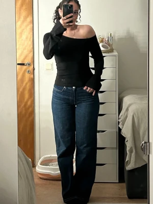 Svart off shoulder topp - Trendig svart off shoulder topp med långa ärmar och figurnära passform. Toppens material är stretchigt och mjukt , perfekt för en stilren look. Ärmsluten är något utsvängda för extra detalj. Passar xs & s!