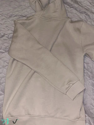 Beige hoodie från Moncler med dragkedja - Snygg beige hoodie från Moncler med dragkedja framtill och klassisk Moncler-logga på bröstet. Hoodien har huva, ribbade muddar och fickor på sidorna. Perfekt för en chill och stilren look. Materialet känns mjukt och skönt mot huden.