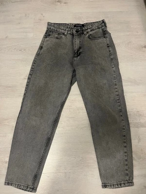 Grå mom jeans från Vamos - Snygga grå mom jeans från Vamos med hög midja och raka ben. Jeansen har klassisk femficksdesign och bälteshällor. Tillverkade i slitstark denim som ger en retro och avslappnad look.