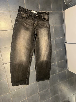 Svarta loose fit jeans med tvättade detaljer - Säljer ett par svarta Balloon loose fit jeans med snygga tvättade och slitna detaljer framtill. Jeansen har fem fickor, och klassisk knappgylf. Materialet är kraftig denim i bomull. Perfekta för en avslappnad och trendig stil.