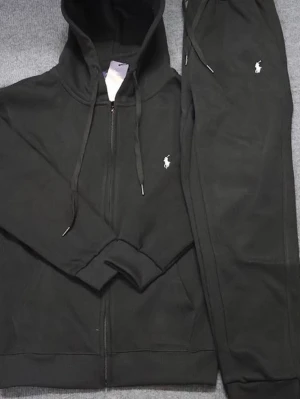 Polo tracksuit - Säljer ett svart set från Polo Ralph Lauren med dragkedja på hoodien och matchande byxor. Båda delarna har den klassiska vita loggan broderad på bröstet och benet. Setet har en sportig look med huva och dragsko, perfekt för en avslappnad stil. Priset är ej skrivit i sten och kan diskuteras, hör av dig om du vill ha fler bilder