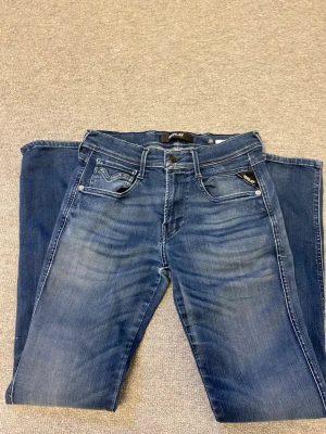 Replay jeans  - Snygga blå slim fit jeans från replay  med klassisk femficksdesign och coola slitningar framtill. Jeansen har kontrastsömmar, bälteshällor och detaljerade bakfickor med broderi. Perfekta för en avslappnad och trendig look.