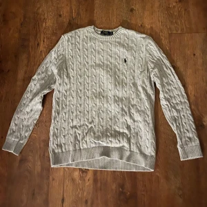 Grå stickad Ralph Lauren  - Säljer en grå kabelstickad tröja från Ralph lauren i storlek M. Tröjan är använd något fåtal gånger men inget som påverkar alls. 