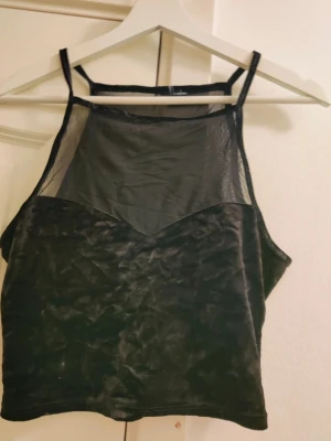 Svart mesh och sammetstopp crop top  - Snygg svart topp med tunna axelband, överdelen är i transparent mesh och resten i mjuk sammetsliknande material. Perfekt för att skapa en edgy och trendig look. Toppen har en cool kontrast mellan mesh och sammet som gör den unik.