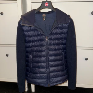 Mörkblå Cardigan från Colmar - Snygg mörkblå Cardigan från Colmar med stickade ärmar och vadderad kropp. Jackan har huva, dragkedja framtill och två fickor. Perfekt nu inför höst tider, men fungerar även väl att användas under vintermånaderna. Köpt på zalando för ny pris för lite mindre än 1 år sen, ny pris(4000)kr. Pris kan diskuteras, och inga defekter. Storlek:48 vilket motsvarar s, men skulle ändå säga att den är lite större en s men för att vara säker kan man få bilder och info om hur den sitter på mig baserat på mig. 