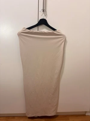 Beige långkjol i mjukt material - Säljer en enkel och stilren beige långkjol i mjukt och stretchigt material. Kjolen har en rak passform och är perfekt för dig som gillar minimalistisk stil. Inga synliga detaljer eller mönster, bara clean och snygg.