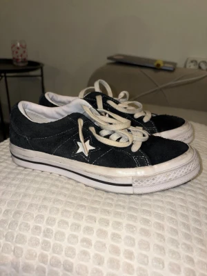 Converse One Star svarta sneakers - Svarta Converse One Star sneakers i mocka med vit stjärndetalj på sidan och vita snören. Klassisk låg modell med vit sula och svarta ränder. Perfekta för en avslappnad och cool stil.