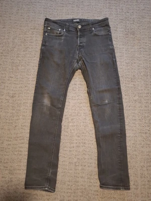 Svart/gråa jeans från Jack & Jones - Säljer ett par svart/gråa Jack & Jones med passform comfort och klassisk femficksdesign, Storlek 29W 32L. Perfekta för dig som gillar en tidlös och enkel stil. Skrive vid frågor.