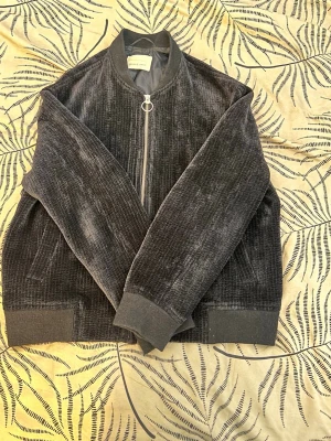 Mörkblå bomberjacka från Weekday - Snygg mörkblå bomberjacka från Weekday med glansig, ribbad yta och silverfärgad dragkedja med ringdetalj. Jackan har ribbade muddar och krage samt ett slätt, mörkblått foder. Perfekt för dig som vill ha en stilren och trendig look.