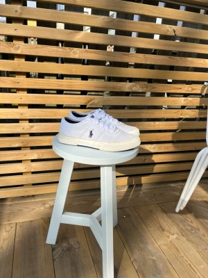 Vita Polo Ralph Lauren sneakers - Snygga vita sneakers från Polo Ralph Lauren med klassisk låg profil. Skorna har vit ovandel i canvas, vit sula och den ikoniska Polo-loggan broderad på sidan. Perfekta för en clean och stilren look. Skön passform och tidlös design.Ny pris 1200 kr!!! 75% mindre än i butik