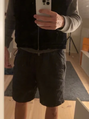 Stenström väst - Säljer en snygg och välgjord väst från Stenströms i storlek M. Västen är i ett mörkt, elegant tyg med lätt struktur som ger ett exklusivt intryck. Den har huva, dragkedja framtill och två praktiska fickor, vilket gör den både stilren och funktionell.  Perfekt att bära över en tröja eller hoodie för en avslappnad men välklädd look. Passar lika bra till vardag som till lite mer uppklädda tillfällen.