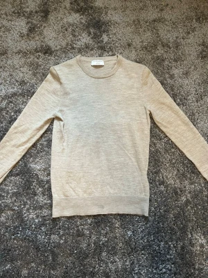 Beige stickad tröja från tiger of Sweden  - Snygg beige stickad tröja från tiger of sweden i tunn ullmix. Tröjan har rund halsringning, långa ärmar och en klassisk, stilren design som passar till det mesta. Perfekt basplagg för lager på lager och enkel att matcha.