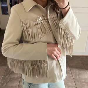 Beige mockajacka med fransar HM h&m storlek S - Säljer en beige mockajacka med långa fransar både fram och på ärmarna. Jackan har klassisk krage, knappar framtill och en loose passform. Perfekt för dig som vill sticka ut med en western-inspirerad look. Storlek 36, normal i storleken. Mycket bra skick, dock finns några få fläckar baktill (se näst sista bilden) som borde gå bort i tvätt och syns knappt när den bärs. 