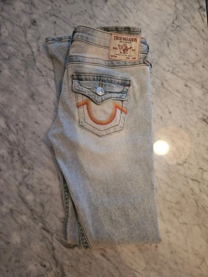 Ljusblå True Religion jeans bootcut - Säljer mina snygga True Religion jeans I modellen joey i storlek 24. Använda bara ett få antal gånger då som inte riktigt passar mig. Köpta för ca 2-3 månader sen, inga synliga defekter och i jätte bra skick.       Köpta för 1600