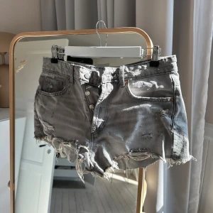 Gråa jeansshorts från Zara - Säljer ett par gråa jeansshorts med slitningar för en edgy look. Shortsen har knappar framtill, Perfekta för sommaren och ger en avslappnad vibe.passar mig som är S/M