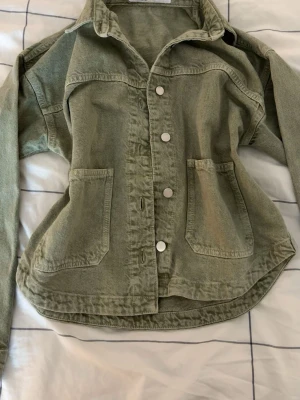 Grön overshirt från ZARA - Snygg grön jeansjacka från ZARA i storlek XS. Tillverkad i ett mjukt bomullstyg med två stora fickor framtill och tryckknappar. Perfekt lager på lager-plagg med avslappnad passform och klassisk krage. 