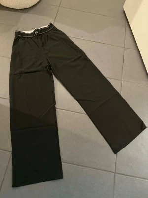 Svarta mjukisbyxor från Alo. Storlek S - Säljer ett par svarta mjukisbyxor från Alo med bred resår i midjan och diskret logga framtill. Byxorna har raka ben och är tillverkade i ett mjukt och stretchigt material som känns skönt mot huden. Perfekta för chill eller träning.