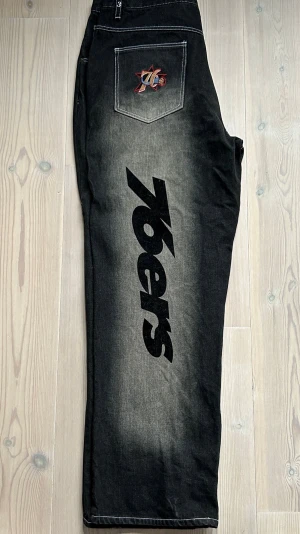 Vintage Unk Denim NBA 76sixers Allen Iverson Jeans - Sällsynta och unika vintage jeans från 90-talet från UNK Denim i samarbete med NBA och Allen Iverson. Storlek 36, långa och raka/baggy - passar mig som är 196cm lång och bär W33. Riktigt cool modell med tydlig 90s-känsla som är svår att hitta idag.   Skicket är överlag mycket bra för sin ålder. Det finns två små hål mellan benen som tidigare har sytts ihop. De syns inte när man bär byxorna och sitter precis vid sömmen. 