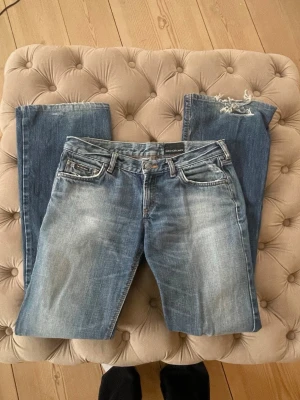 Low waist bootcut jeans - Säljer ett par blå jeans från Calvin Klein med slitningar och distressed detaljer. Klassisk femficksmodell med raka ben och ljus tvätt. Jeansen har en läderpatch med logga bak i midjan och är tillverkade i denim.