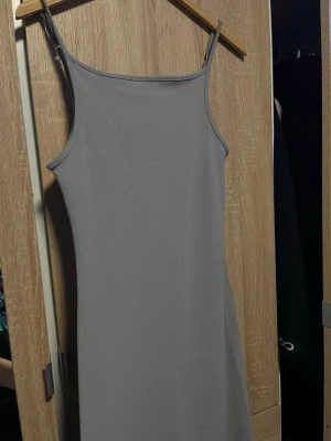 Grå ärmlös långklänning - En stilren grå långklänning med smala axelband och rak halsringning. Klänningen har en minimalistisk design utan mönster eller extra detaljer, vilket gör den enkel att styla. Materialet ser ut att vara mjukt och följsamt, perfekt för en clean look. Från H&M  använt 1 gång  , jätte FIN , köpte för 300 