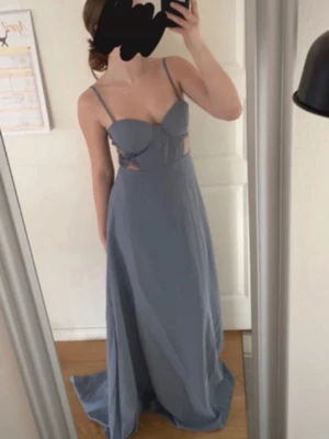 Ljusblå långklänning med spetsdetaljer - Elegant ljusblå långklänning med tunna axelband och spetsdetaljer vid sidorna. Klänningen har en figurnära överdel med kupor och öppen rygg, samt ett svepande, långt fall. Perfekt för speciella tillfällen. Har klänningen i storlek S och M. Aldrig använda