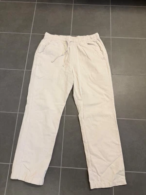 Beiga linnebyxor från Lager 157, stl M - Säljer ett par beiga linnebyxor med avslappnad passform och resår i midjan samt dragsko. Byxorna har två sidofickor och raka ben. Perfekta för en chill och stilren look.