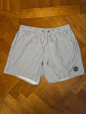 Mönstrade badbyxor från Colmar - Säljer ett par vita badbyxor från Colmar med blått grafiskt mönster. De har elastisk midja med dragsko och en liten rund logotyp på vänster ben. Perfekta för stranden eller poolen fråga gärna för bättre bilder nypris 1399kr