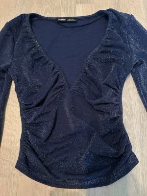 Mörkblå glittrig topp från pull&bear - Snygg mörkblå topp från pull&bear med glittrigt tyg och v-ringad urringning. Toppen har långa ärmar och figurnära passform, perfekt för fest! Materialet känns mjukt och stretchigt.💕💕