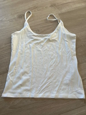Vit linnetopp från Gina Tricot - En enkel och stilren vit linnetopp från Gina Tricot med tunna axelband. Perfekt att matcha med jeans eller kjol. Tillverkad i mjuk bomull för en skön känsla hela dagen.