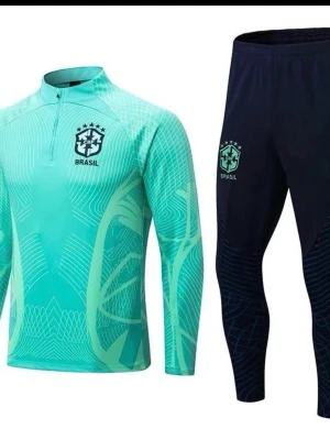 Nike Brasil träningsset mintgrön/svart - Snyggt träningsset från Nike med Brasil-logga. Tröjan är mintgrön med grafiskt mönster, halv dragkedja och lång ärm. Byxorna är svarta med matchande Brasil-märke och smal passform. Perfekt för fotbollsträning eller gymmet.