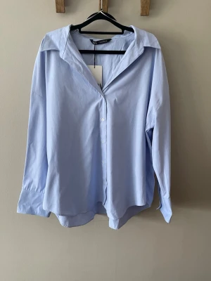 Ljusblå skjorta  - Snygg ljusblå skjorta från Zara. Har en oversized passform med v-ringning. Säljer då jag tog fel storlek och inte hann lämna tillbaka