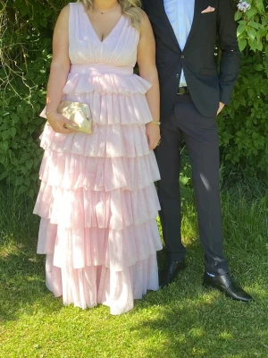 Ljusrosa volangklänning med v-ringning - Säljer en lång, ljusrosa klänning med flera lager volanger och djup v-ringning. Klänningen har breda axelband och markerad midja. Perfekt för bal eller bröllop. Använts en gång.