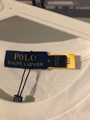 Vit t-shirt från Polo Ralph Lauren - Klassisk vit t-shirt från Polo Ralph Lauren med den ikoniska broderade loggan på bröstet. T-shirten har rund hals och är tillverkad i mjuk bomull för en skön känsla. Perfekt basplagg med stilren design.